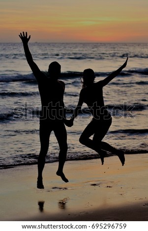 A couple jumping with joy at sunset on the beach.