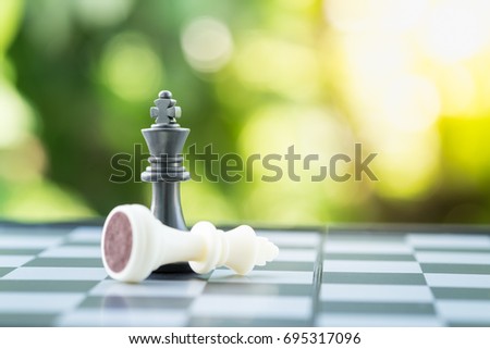 Board game, business and planning concept. Close up of black and white chess king pieces on chessboard with green nature background.
