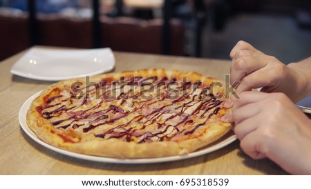 Woman's hands taking pizza slice in cafe.