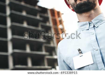 Blank white blank card or business card badge on chest of young architect or engineer on background of a construction site
