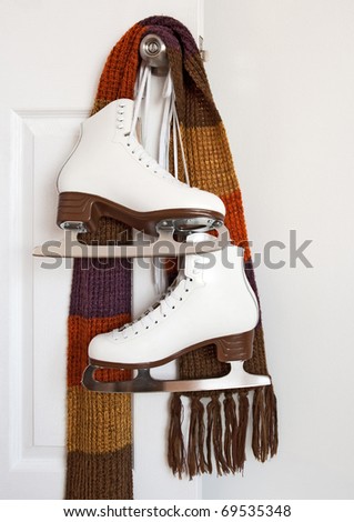 Elegant white figure skates and colourful scarf hanging on a door knob.