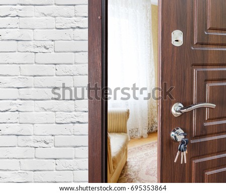 Half opened door, entrance to a living room. Welcome, privacy concept. Door lock with keys, white brick wall, modern interior design.