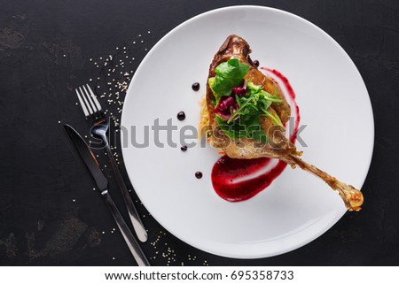 Exclusive restaurant meals. Duck confit with braised cabbage, baked apple and cranberry sauce served on snow white plate with cutlery on black table background, copy space, top view