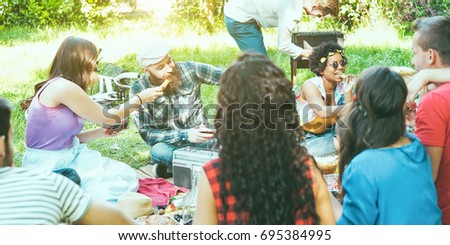 Happy friends making picnic barbecue outdoor in nature park - Young people having fun at bbq party sitting on grass - Food and youth concept - Focus on afro girl and bearded man - Retro camera filter