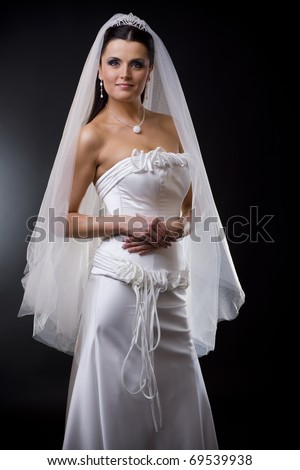 Studio portrait of a young bride wearing white wedding dress with veil, smiling and looking at camera.