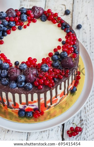Bright festive cake with berries and chocolate on a white wooden background.