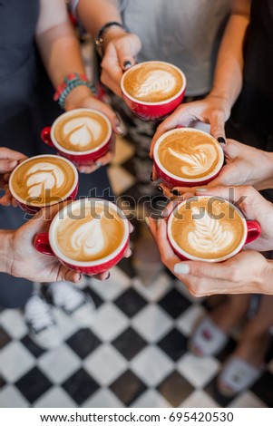 Morning coffee in hands with pictured foam red cups with black and white floor tile background  