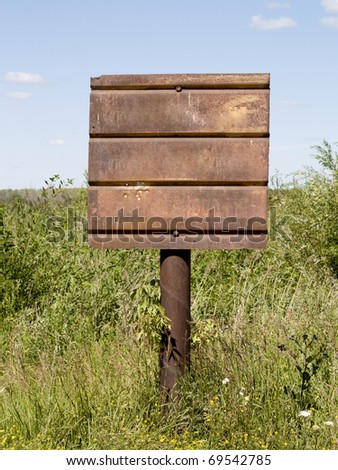 rusty signboard on a pillar, surrounded by green grass