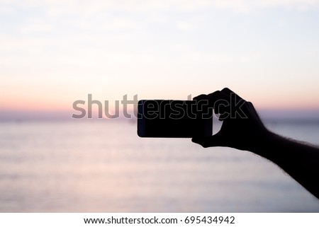 silhouette hand holding smartphone take photo at sunset.