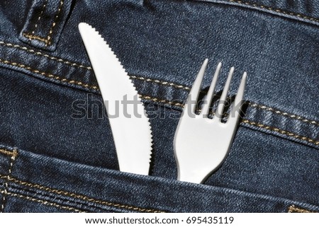 White plastic fork and knife into sea blue jeans pocket. Closeup. Always can get food. Picnic, barbecue, meal. Symbol background