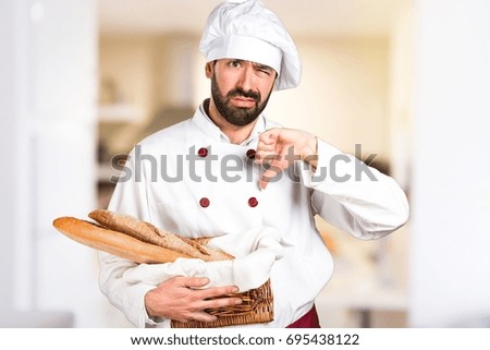 Young baker holding some bread and making bad signal in the kitchen