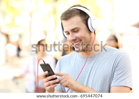 Happy boy listening to music and selecting a song walking on the street