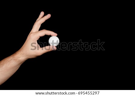 male hand holding between his fingers a ball for ping-pong isolated on black background. the concept of the sport of table tennis Royalty-Free Stock Photo #695455297
