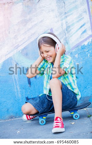 Cute boy with skateboard outdoors, standing on the street with different colorful graffiti on the walls, hipster style, cool fashion