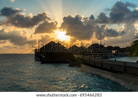 Horizontal picture of yellow beautiful sunset  over bungalows with cloudy sky in Maldives.