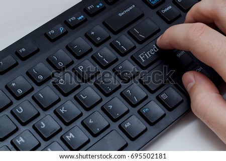 White hand is typing on a black keyboard, a key with the word fired