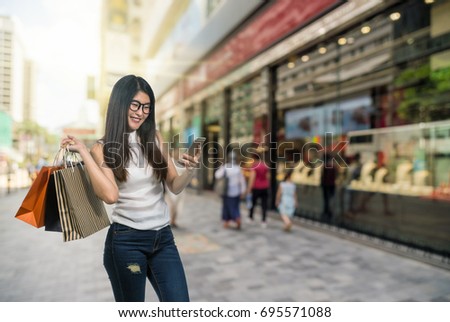 Happy young asian woman shopping in happy feeling and holding the product paper bag over Abstract blurred photo of shopping store in outdoor store mall with people walking street, shopping concept