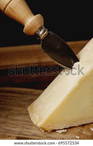 piece of Italian parmesan cheese with a knife.  wood background