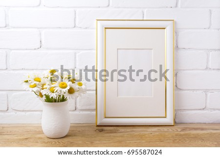 Gold decorated frame mockup with white field chamomile bouquet in handmade rustic vase. Empty frame mock up for presentation artwork. Template framing for modern art.