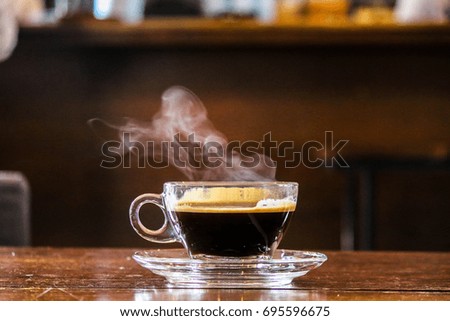 Hot black coffee in glass cup with smoke on wooden table.