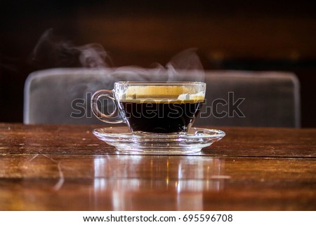 Hot black coffee in glass cup with smoke on wooden table.