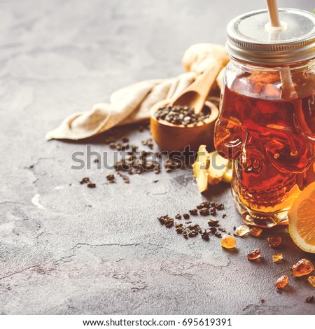 Chinese tea with lemon ginger in a skull jar for halloween day. Holiday festive decoration on a black table. Warm drink beverage infusion for cold flu fall winter days, copy space background, toned