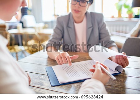 Close-up shot of confident middle-aged entrepreneur pointing her client where to sign contract while having meeting at cozy coffeehouse