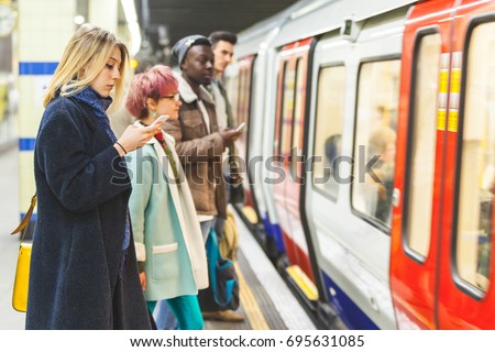 People waiting for the train at subway station. Mixed race persons, two men and two women, staying on a line and waiting to board the train. Commuting and transport Royalty-Free Stock Photo #695631085