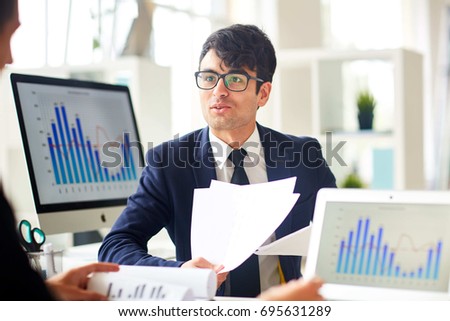 Young economist talking to colleague and explaining financial papers Royalty-Free Stock Photo #695631289