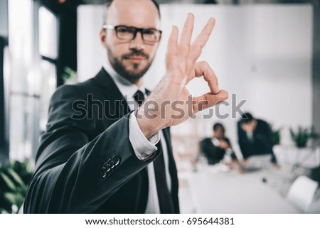 handsome young businessman showing okay sign with blurred colleagues on background