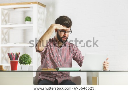 Portrait of crazy young businessman looking into the distance while sitting at modern office desktop with laptop and other items. Leisure concept 
