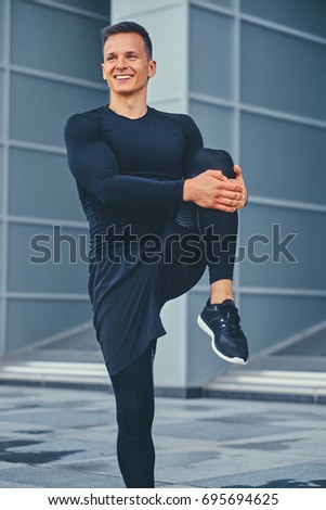 Sporty athletic male is warming up and stretching outdoors over modern building background.