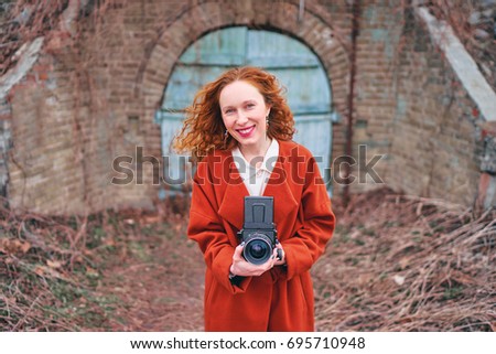 Pretty photographer. Long hair young woman with old fashioned camera taking pictures outdoors