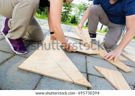 Low Section Of Friends Solving Wooden Planks Puzzle On Patio