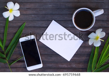 Flat lay with white paper and bamboo leaves on wooden background. Coffee cup on rustic wood. Black screen smartphone. Tropical vacation scene or header. Exotic island lifestyle flat lay. Iphone mockup