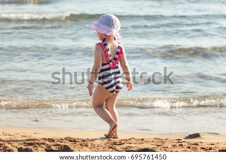 Cute little girl standing on summer beach at sunset and looking to sea
