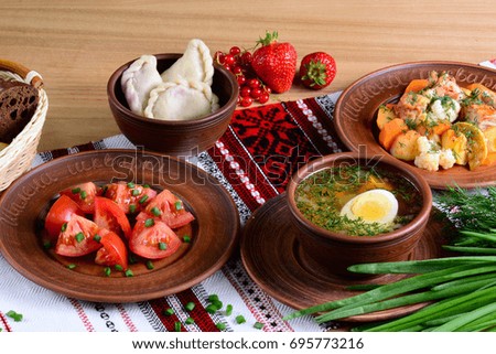 National dinner of Ukraine: vegetable soup with boiled egg, salad with tomatoes in sunflower oil, vareniki with berries, vegetable ragout with tablecloth on a wooden table.