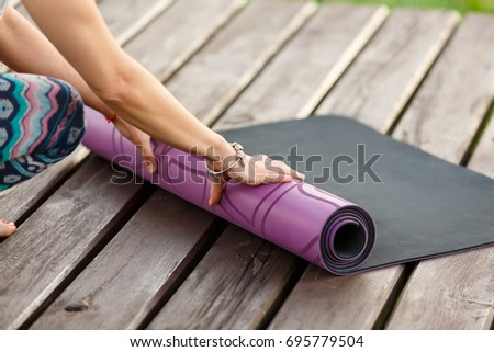 Close-up of young woman hands folding yoga or fitness mat after working out at wooden floor at terrace. Healthy life, keeping fit concepts.