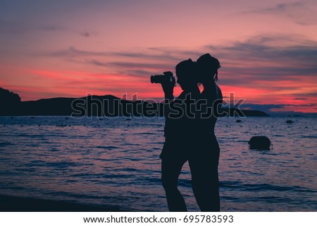 Silhouette couples are taking photos on the beach. Sunset background