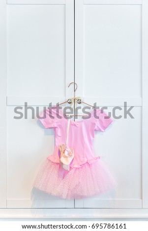 Beautiful children wear pink dress with white dotted chiffon skirt and orange color cloth shoes hanger on white wooden wardrobe for pretty girl in celebration party.