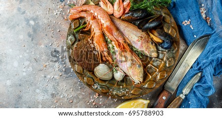 Image of fresh seafood on ceramic plate on table with lemon, knives, seashells