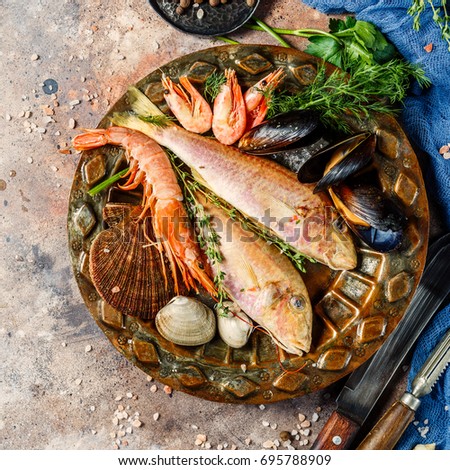Fish, shrimp, clams on plate at table with blue cloth, spices, knives