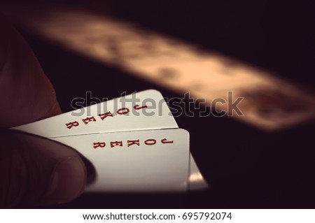 Hand with two playing cards showing jokers over a black background