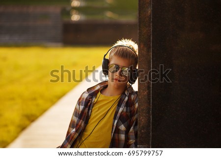Handsome teenage boy in plaid shirt listening to music and using phone on sunset