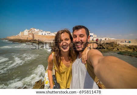 Beautiful tourist couple smiling and taking photo selfie with Cityscape of Essaouira, a UNESCO world heritage site in Morocco. North Africa