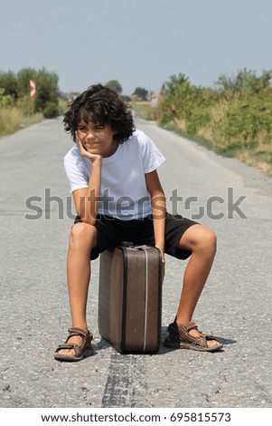 A scene with a curly haired boy with an old suitcase who is waiting on the road, expressions