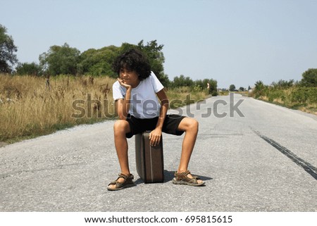 A scene with a curly haired boy with an old suitcase who is waiting on the road, expressions