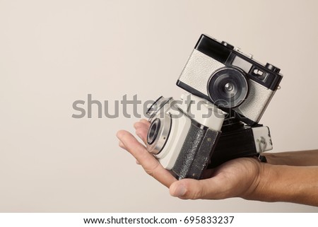closeup of a young man with a pile of old film cameras in his hands, against an off-white background with a blank space on the left