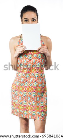 Playful woman is holding blank paper. The empty card is covering the mouth. Woman with short curly hair wearing colorful dress. Summer and tropical concept. Isolated on white background.