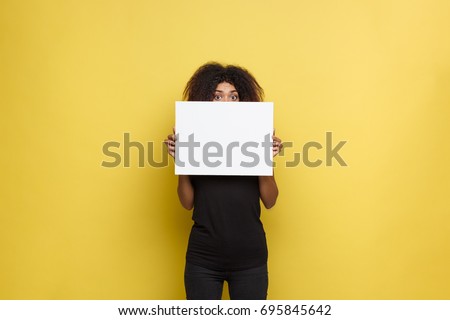 Business Concept - Close up Portrait young beautiful attractive African American smiling showing plain white blank sign. Yellow Pastel studio Background. Copy space.